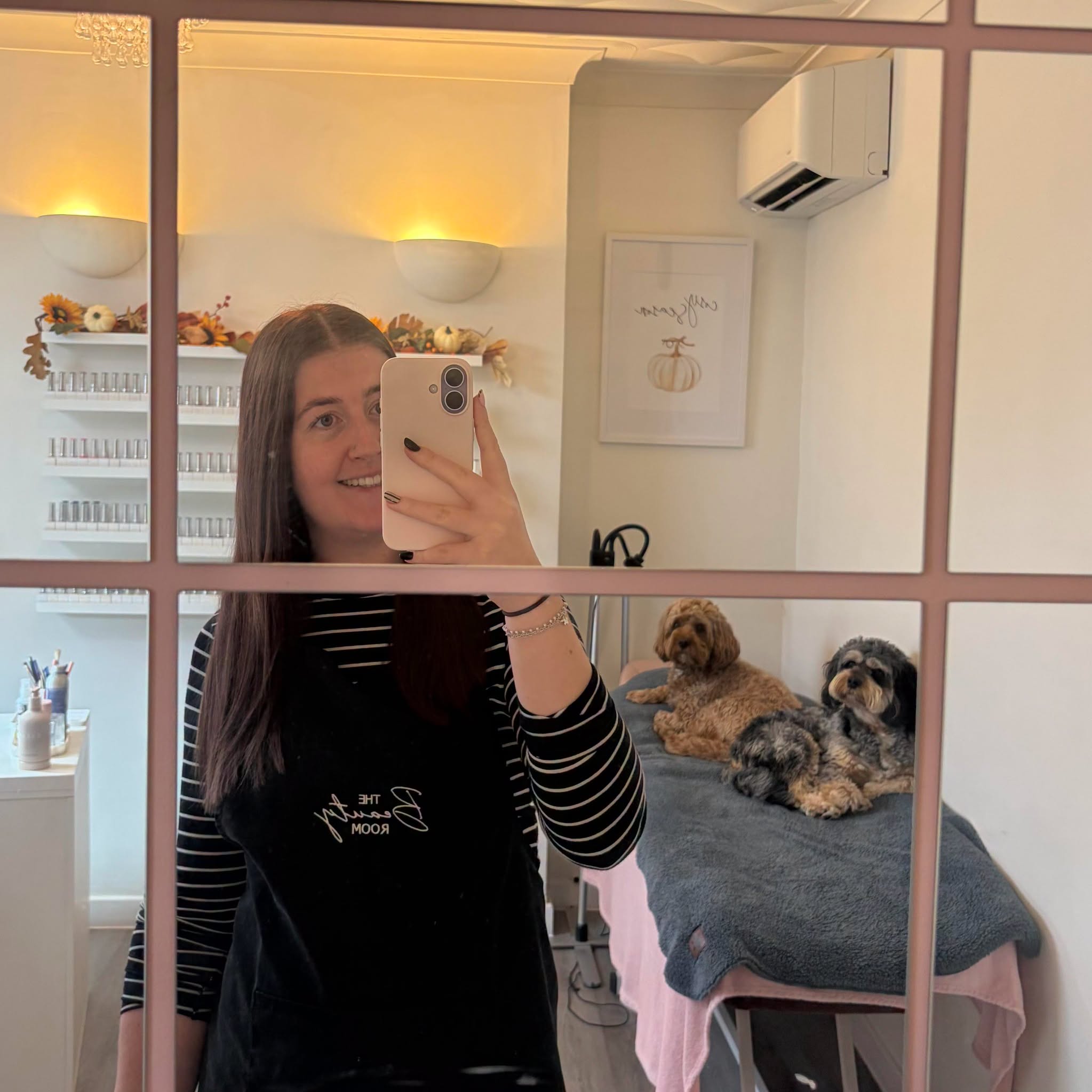 Chloe in the salon wearing her Beauty Room apron, with the two salon dogs resting behind her
